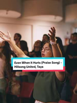 The image captures a woman in an indoor setting with arms raised in worship, surrounded by other individuals. A text overlay in a rectangular banner provides additional context.
