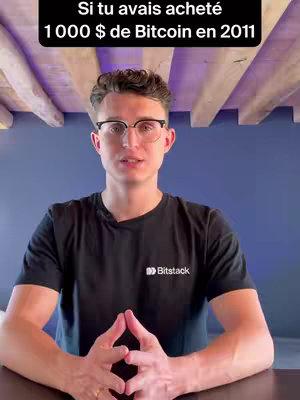 A man in a black t-shirt and glasses is positioned in front of a blue wall. Text overlayed on top of the image asks, \"Si tu avais acheté 1 000 $ de Bitcoin en 2011\". The man is looking directly at the camera and has his hands clasped together.