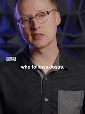 A medium shot of a man with short, light-colored hair and glasses, looking towards the camera. He's wearing a dark, button-down shirt with a grey collar. Text overlays are added at the bottom of the frame.