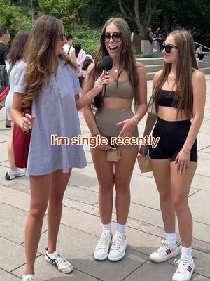 Three young women are standing outside on a sunny day. The woman in the center is holding a microphone and wearing sunglasses, with text overlayed on the cover image.