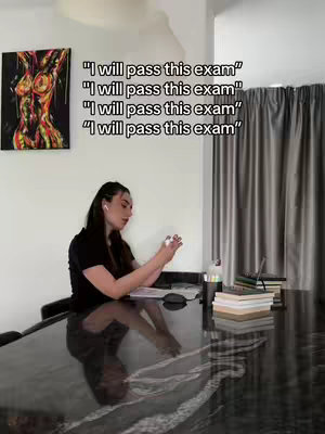A young woman sits at a table with a laptop, books, and study materials, aiming to create an image of aspiration and determination. Above her appears an art piece and motivational overlay text.