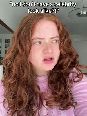 A young woman with auburn curly hair is in the center of a medium shot, looking off to the side with a concerned expression. "no i don't have a celebrity look alike?!" floats at the top on a black background