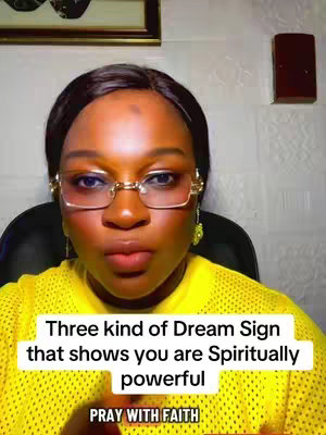 A close-up shot of a woman with dark hair and glasses, wearing a yellow shirt. She is centered in the frame, looking directly at the camera. Text overlays the bottom of the image. The background is a simple wall with a framed picture.