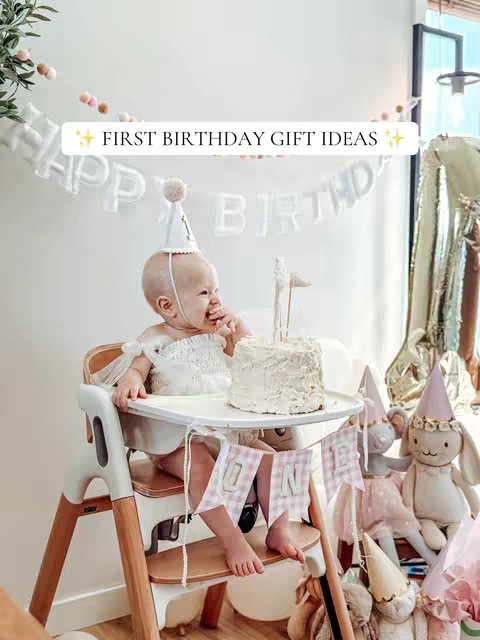A baby girl sits in a high chair in front of a decorated wall, with a cake in front of her. The scene is lit with natural light, and the color palette is soft and neutral.
