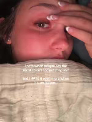 A close-up shot of a person's face, mostly covering their eyes and part of their nose. The person's face is flushed red. The person is holding their hand up to their face and there is overlayed text. The background is a patterned pillow.