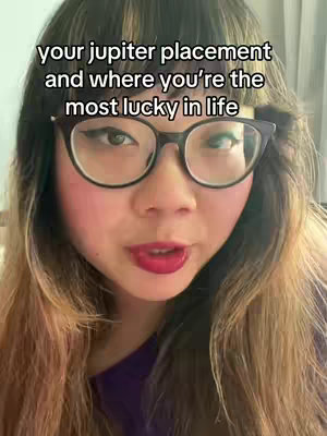 A medium shot shows a woman with long, wavy hair. She wears glasses and has makeup on, with a purple top. The text overlay at the top reads, 'your jupiter placement and where you're the most lucky in life'.