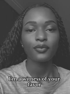 A grayscale, close-up portrait of a person's face. The person has dark skin, braided hair, and is looking directly at the camera with a serious expression. The text overlay at the bottom says, 'I'm a witness of your favor'.