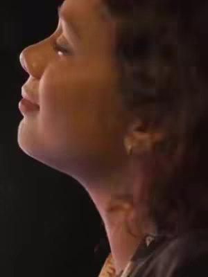 A close-up shot from the side showing the upper half of a person's face. The person's head is tilted upwards with their eyes closed. The skin tone appears to be light brown. The background is a dark, undefined color. The person is wearing a dark-colored outfit.
