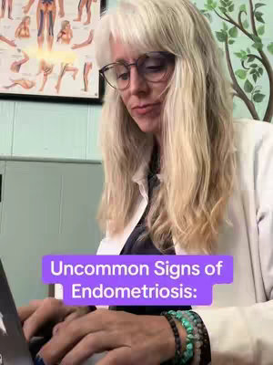 An adult female with long, blonde hair and glasses is seated, looking down at a laptop; in the background, there is a poster with anatomical diagrams, and text in a purple rectangle overlay.