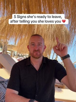 A middle-aged man with a ginger beard and short hair sits on a beach chair, pointing upwards with his right index finger. The background shows a beach with greenery, bright sunlight, and seating areas. Text overlay highlights the video's theme in a white rectangular box at top.
