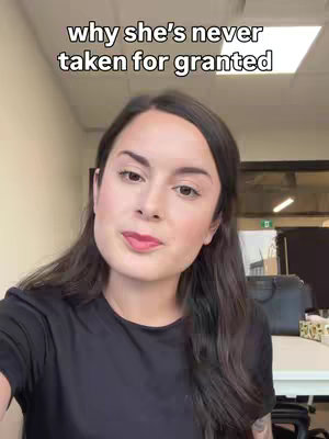 A woman with long, dark hair is centered in a video frame. Her face is mostly visible, with a slight smile and a subtle red lipstick. She's wearing a black top, and the background features an office setting. Text above the woman reads 'why she's never taken for granted.'