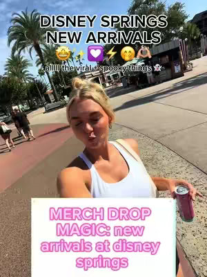 A selfie-style shot at Disney Springs with the creator facing the camera, making a kissing face. Text overlays include "DISNEY SPRINGS NEW ARRIVALS" at the top, and "MERCH DROP MAGIC: new arrivals at disney springs" at the bottom. The background shows a sunny outdoor setting with shops and palm trees, and the creator is holding a can with a drink.