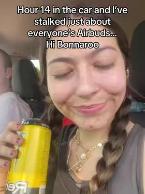 A selfie-style video taken from inside a car. The main subject is a woman with her brown hair pulled back into two braids; she is holding a yellow beverage. Text overlays the image, written in white font, with a black background.