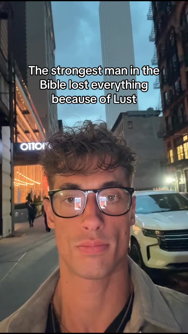 A man wearing glasses is centered in the frame, with the background showing urban architecture and a partial view of a white SUV. Text is overlaid at the top.