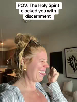 A woman with blonde hair pulled back in a clip sticks out her tongue and makes a face. Text in a white box on the image reads 'POV: The Holy Spirit clocked you with discernment.' The background shows a room with some furniture.