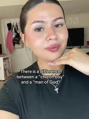 A woman with a light complexion is the focus of the shot, positioned against a softly lit background. Her gaze is directed towards the camera, engaging the viewer. She's wearing a dark, likely black, top and has her hair styled neatly. Her face is framed by a well-lit environment, enhancing the details of her makeup, including visible eye makeup and lip gloss. Text overlay at the bottom states: There is a difference between a "church boy" and a "man of God".