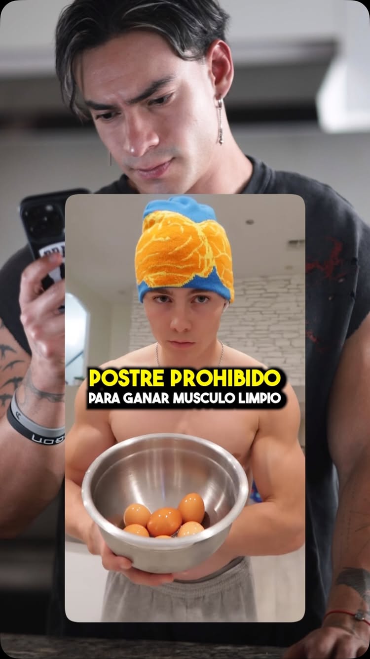 The cover image shows a man holding a phone and looking at the camera, he is wearing a black top and has a tattoo on his arm. Behind him, there's a man wearing a towel on his head holding a bowl with eggs in a kitchen setting. The overlay text reads: "POSTRE PROHIBIDO PARA GANAR MUSCULO LIMPIO (Mousse De Chocolate Viral) ¿VALE LA PENA? 🤢🚨💪🏼 ".