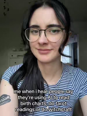 A woman with dark hair and glasses is shown from the chest up, smiling gently. She wears a blue and white striped shirt in front of a blurred background. The text overlay reads "Me when I hear people say they're using AI to read birth charts, do tarot readings or do witchcraft".