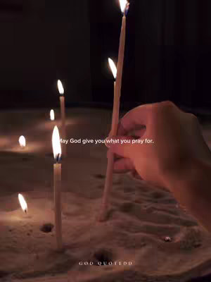 A close-up shot of candles lit in an indoor setting. The scene is dimly lit with a focus on the candles, flames are the main source of light. In the foreground, a hand is seen holding a candle towards the flame. The layout is simple, focusing on the candles and the hand interacting with them, creating a sense of warmth and spirituality.