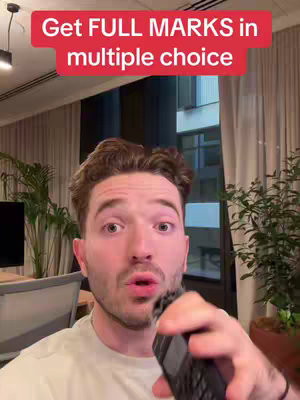 A man with wavy brown hair is indoors, looking at the camera and speaking, most likely presenting to an audience of viewers. He has a slight smile and is holding what appears to be a small handheld device.