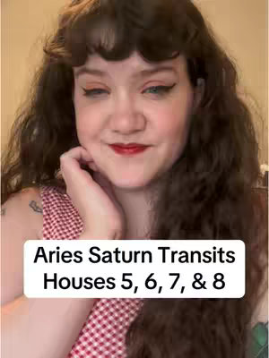 A woman with curly brown hair and red lipstick is the central figure, positioned against an illuminated background. The foreground features a white rectangular text box with the words "Aries Saturn Transits Houses 5, 6, 7, & 8" in a bold black font. The woman supports her chin with her left hand. Her facial expression is a mix between a smile and a serious look.