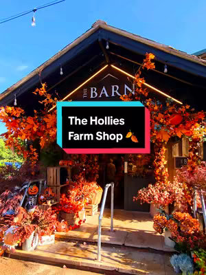 An image showing the facade of a farm shop decorated for autumn. The shop's entrance is framed with autumn leaves and foliage, and a sign reads "The Barn". A rectangular text box overlays the image, displaying the name of the shop and a leaf icon, overlaying the scene.