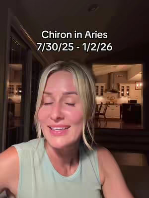 A woman with blonde hair wearing a light green tank top is in the foreground, softly smiling with her eyes closed. Behind her is a dark room with a view of a bright kitchen and outdoor area. Text overlay reads, 'Chiron in Aries 7/30/25 - 1/2/26'.