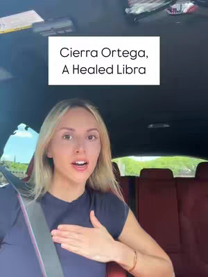 A woman with blonde hair is seated in the driver's seat of a car, looking at the camera. A white box overlay reads 'Cierra Ortega, A Healed Libra'. The car interior is black with red seats. The scene suggests a casual, conversational video.