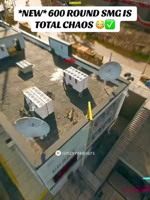 An overhead shot from a first-person perspective of a rooftop in a video game. The main focus is on a rectangular building with several structures. There are multiple shipping containers, and a parachute-deploy indicator with a downward arrow.