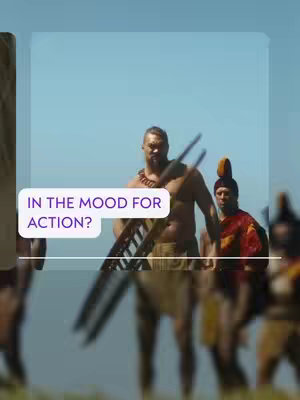 The image is a vertical composition, set outdoors. The foreground features a muscular man holding a weapon and wearing a traditional outfit. Behind him is a line of other men, also dressed in costumes, some with feathered headdresses, suggesting a cultural or historical setting. The background shows a clear blue sky and a grassy area.