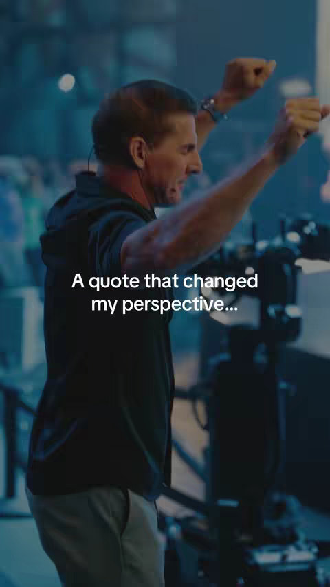 A man with short hair raises both arms in the air with a stage-like background. The text overlay reads "A quote that changed my perspective..."
