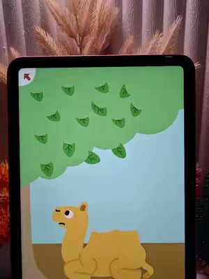 The video cover displays a tablet screen showing a cartoon image of a camel looking downwards with a sad expression, standing under a green tree. The screen sits on a wooden surface, and behind it, a curtain and decorative plants provide a soft background.