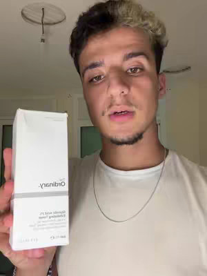A young man is holding a white box in front of him. The box has the words 'ordinary' written on it in black. He is smiling and looking at the camera. The background is a room.