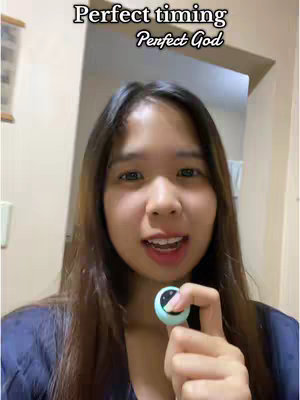 A woman faces the camera in a well-lit indoor setting, holding a small circular device. She's smiling with her mouth open. Text overlays at the top of the frame read "Perfect timing" and "Perfect God."