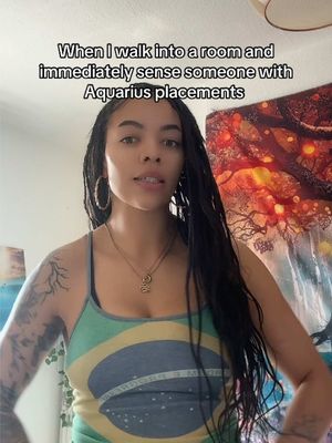 A woman with long, dark hair that is styled in dreadlocks is the central figure. She is wearing a tank top with the colors of the Brazilian flag. The background is warmly lit, featuring a tapestry with a design of oranges and reds. Above her, there is a text overlay in a black font.