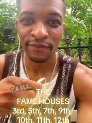 A selfie-style shot of a man in a park setting, looking closely at the camera. He wears a white tank top under a brown and patterned vest. Text overlays are present, with a logo on his finger and list of astrological houses.