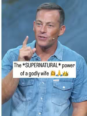 A man with short, styled hair and a blue button-down shirt is speaking into a microphone. A white text box overlay features the text 'The *SUPERNATURAL* power of a godly wife' along with emoji.