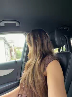 The video cover shows the interior of a car. A woman with long brown hair is sitting in the driver's seat, turned towards the side. The car's interior is dark with visible seat, door and handle. The houses and trees are visible in background through the window in the left side.