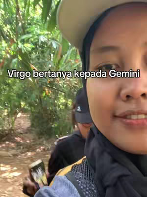 A selfie shot where the creator is in the foreground, with a forested landscape in the background. The creator is wearing a hat and a dark scarf around her neck. Adjacent to the Creator are other people.