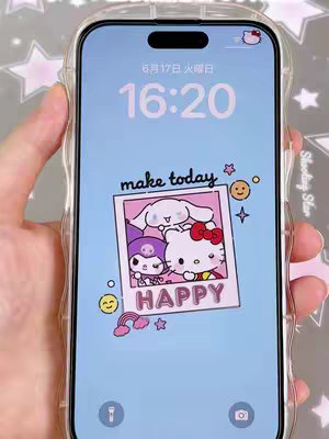 A smartphone screen displaying a lock screen with a Sanrio-themed live wallpaper. The wallpaper features a light blue background with a time display at the top, and a cartoon framed photo in the center. The photo frame contains characters from Sanrio, centered around a Hello Kitty, with text that reads 'HAPPY'. The phone is held by a hand in a clear protective case, and the background hints at a starry motif.