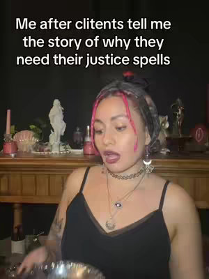 A woman with pink-streaked hair and a headscarf stands in front of a shelf adorned with religious and decorative items, with text overlayed, 'Me after clitents tell me the story of why they need their justice spells'.