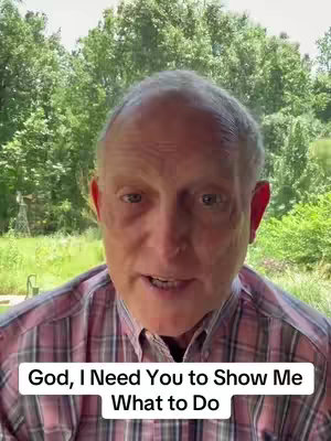 A middle-aged man with thinning hair and a collared shirt is centered in the frame, speaking directly towards the camera. The background reveals a lush green environment, suggesting an outdoor setting.