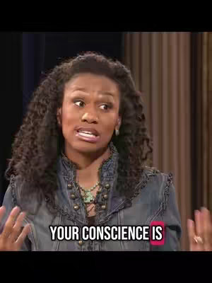 A woman with curly dark hair is speaking. She is wearing a denim jacket and a necklace. Text overlayed reads, "YOUR CONSCIENCE IS". The background is blurred, suggesting a studio or stage setting.