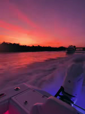 The cover image captures a vibrant sunset over a body of water with a boat in the foreground. The sky is filled with shades of orange and pink, suggesting a post-sunset or pre-sunrise moment. The water reflects the colors of the sky, adding to the warm, colorful composition. The boat's interior is visible, with the edge of the boat and its mechanical components illuminated with blue and pink lights. The image has a serene and picturesque ambiance.