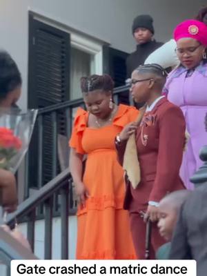 The image captures a candid scene at what appears to be a matric dance, showcasing a group of people on a porch. The central focus is on several women in formal attire, with one in an orange dress and another in a maroon suit carrying a walking stick. The overall composition offers a snapshot of a social gathering.