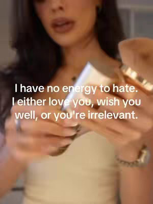A woman is shown from the chest up, holding a white bottle towards the camera. Text that reads "I have no energy to hate. I either love you, wish you well, or you're irrelevant" is overlaid on the image in a white font.