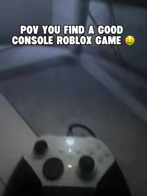The image shows a first-person view of a white and black game controller, likely a console controller. The background is a blurred, shadowed environment, with text overlaid at the top, which indicates the point of view.