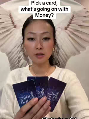 A woman holds three tarot cards, positioned in front of her. Behind the woman, a white, wing-like design is prominently displayed. Above the woman, text reads, 'Pick a card, what's going on with Money?'