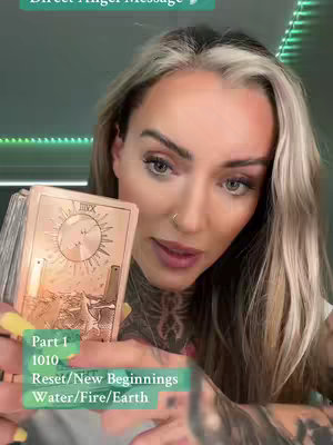A woman with blonde and silver hair with tattoos is holding a tarot card and looking at the camera with engaging expression. The background is a soft green color with subtle lighting. Text overlays are added to describe the video's content; the background is dimly lit.