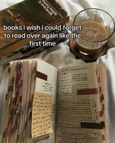 The image presents an open book with several tabs and handwritten notes, beside a stack of books with the title "Wuthering Heights" visible, a glass of iced coffee, and a light-colored blanket or sheet providing the background.
